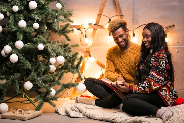 Pareja afroamericana sentada junto al árbol de Navidad