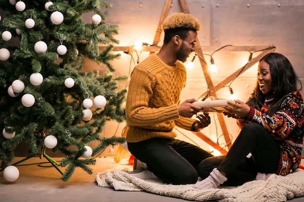 Pareja afroamericana sentada junto al árbol de Navidad