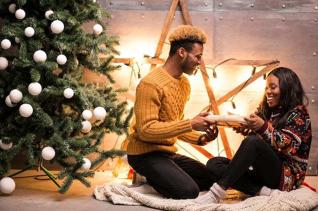 Pareja afroamericana sentada junto al árbol de Navidad