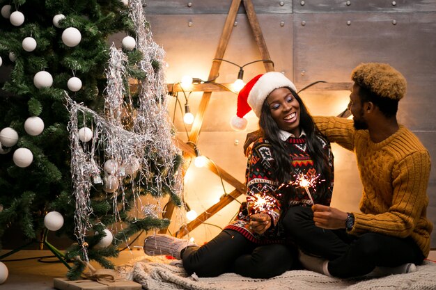 Pareja afroamericana, sentado, con, luces de bengala, por, el, árbol de navidad