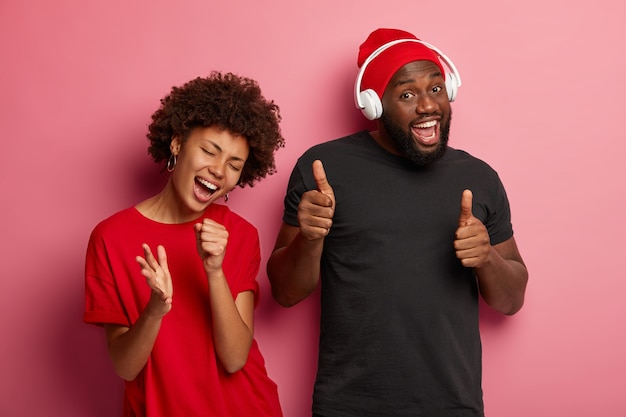 La pareja afroamericana tiene caras felices y relajadas, escucha la melodía y le gusta la pista, se divierte en la fiesta, disfruta de una melodía genial para bailar, la mujer canta junto con la música