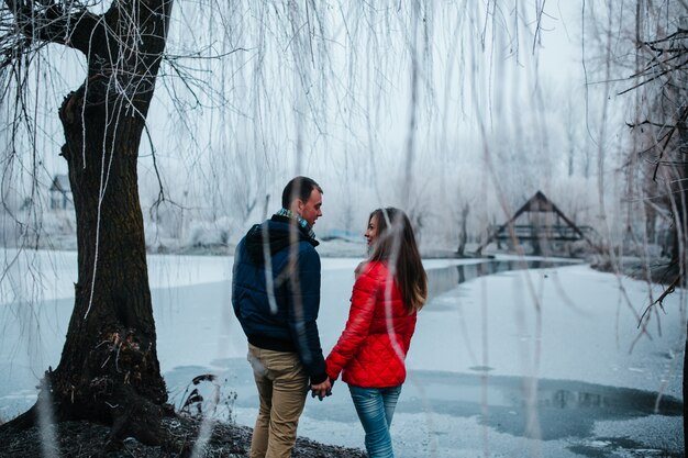 Pareja agarrada de la mano bajo un árbol nevado