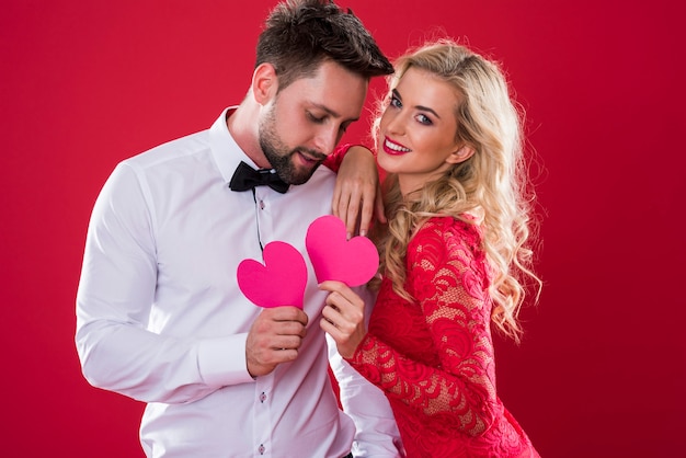 Foto gratuita pareja alegre con corazones de papel rosa