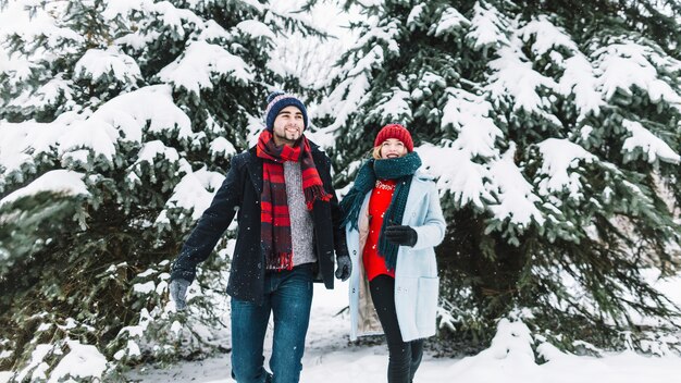 Pareja alegre corriendo en el bosque de invierno