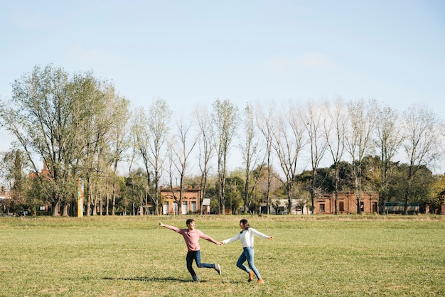 Pareja alegre corriendo por el campo tomados de la mano