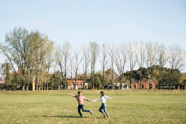 Pareja alegre corriendo por el campo tomados de la mano