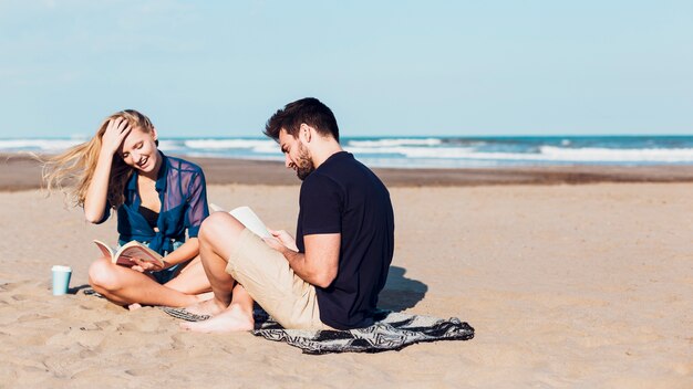 Pareja alegre leyendo libros en la playa