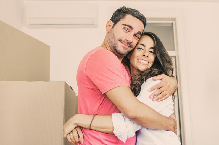 Foto gratuito pareja alegre mudándose a piso nuevo, de pie entre cajas de cartón y abrazándose