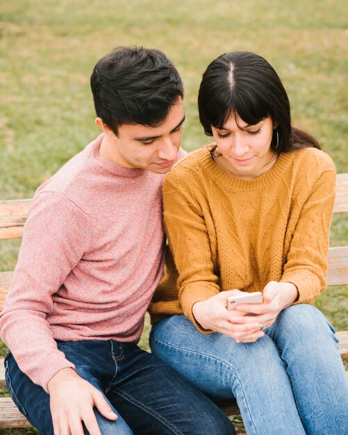 Pareja alegre en el parque mirando el teléfono