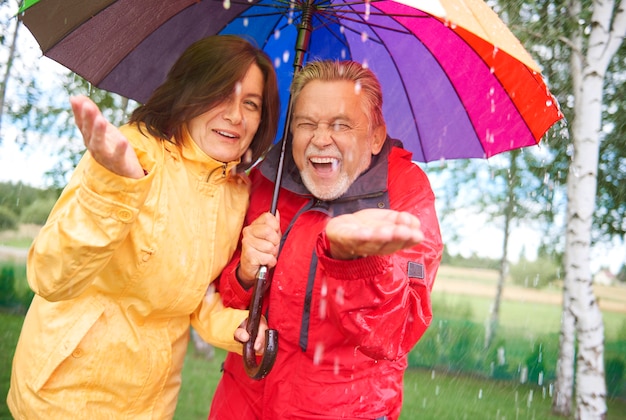 Pareja alegre de pie bajo la lluvia de otoño con paraguas