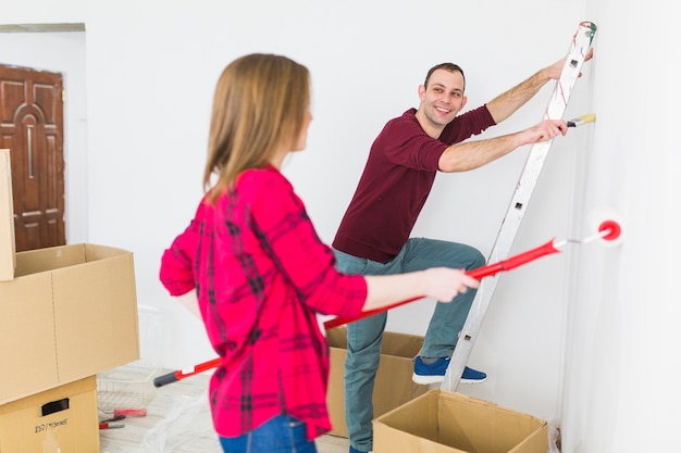 Pareja alegre pintando paredes en el apartamento