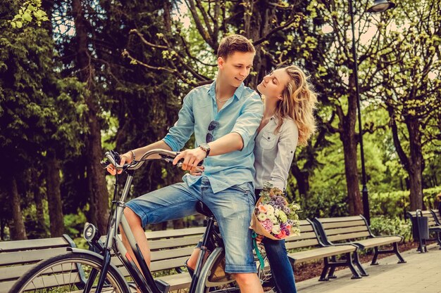 Una pareja alegre posando en una bicicleta en un parque de verano de la ciudad.