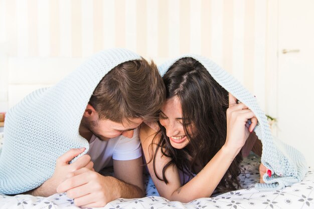 Pareja alegre que miente debajo de la manta