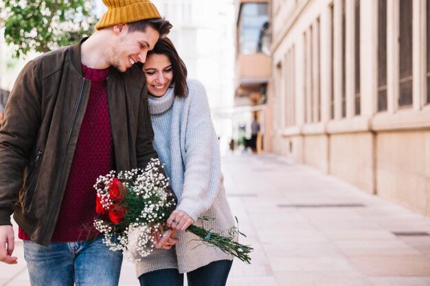 Pareja alegre con ramo caminando por la calle