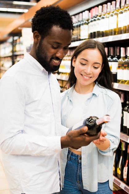 Pareja alegre recogiendo vino en la tienda de comestibles