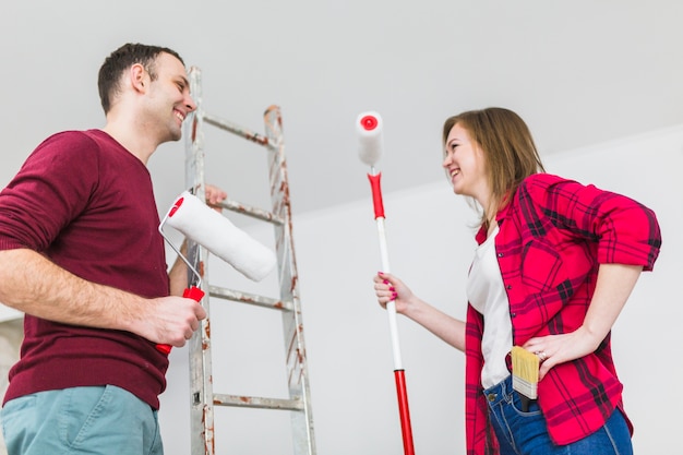 Pareja alegre con rodillos de pintura y escalera