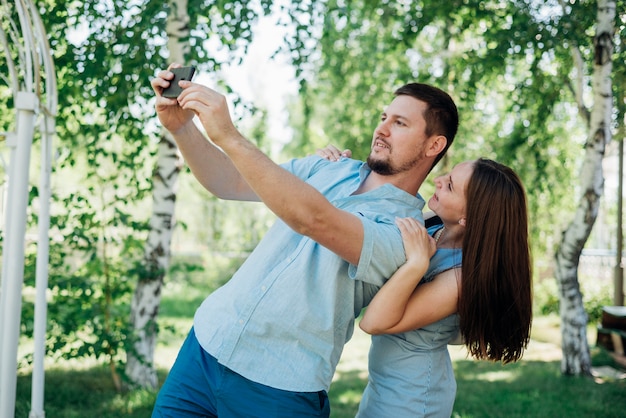 Pareja alegre tomando selfie en bosque de abedules