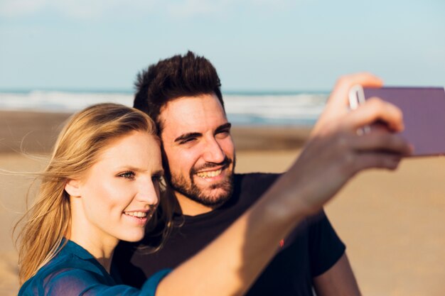 Pareja alegre tomando selfie en la playa