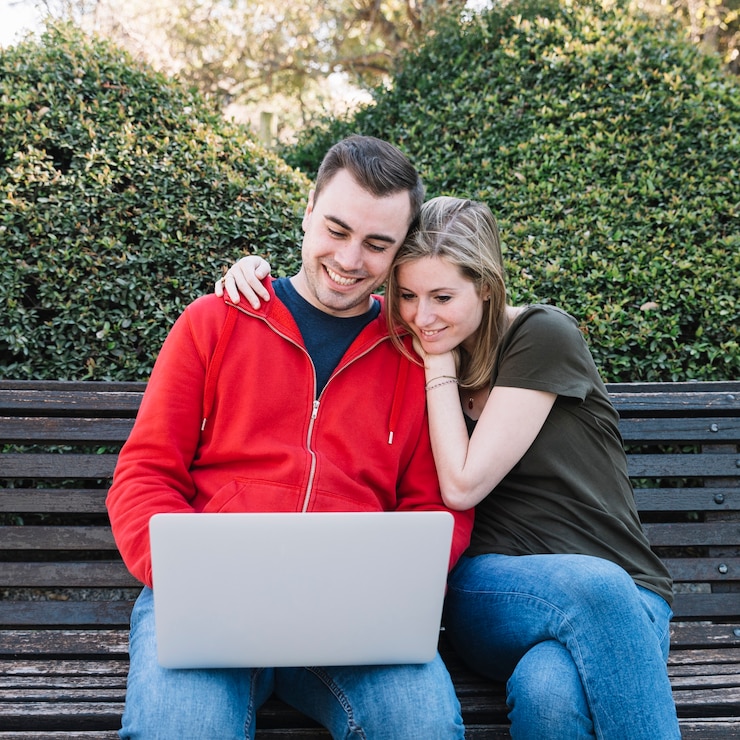 Foto gratuito pareja alegre usando la computadora portátil en el banco