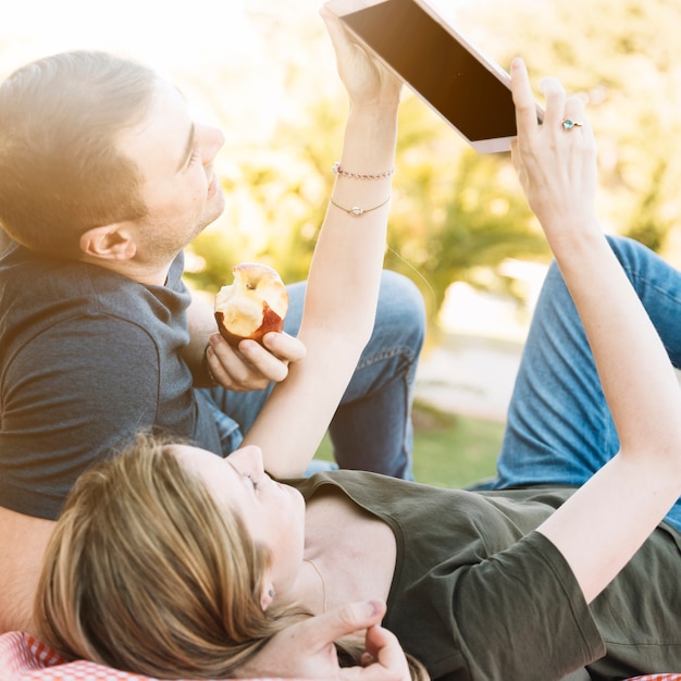 Foto gratuita pareja alegre usando tableta en picnic