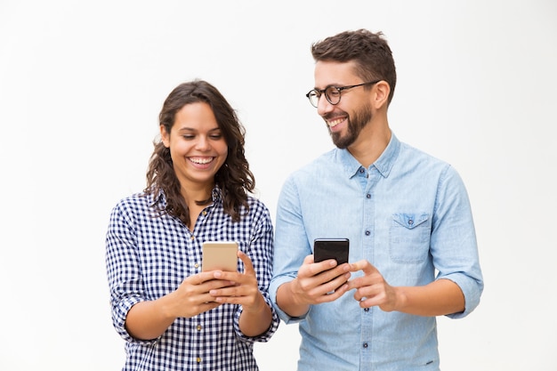 Pareja alegre usando teléfonos inteligentes