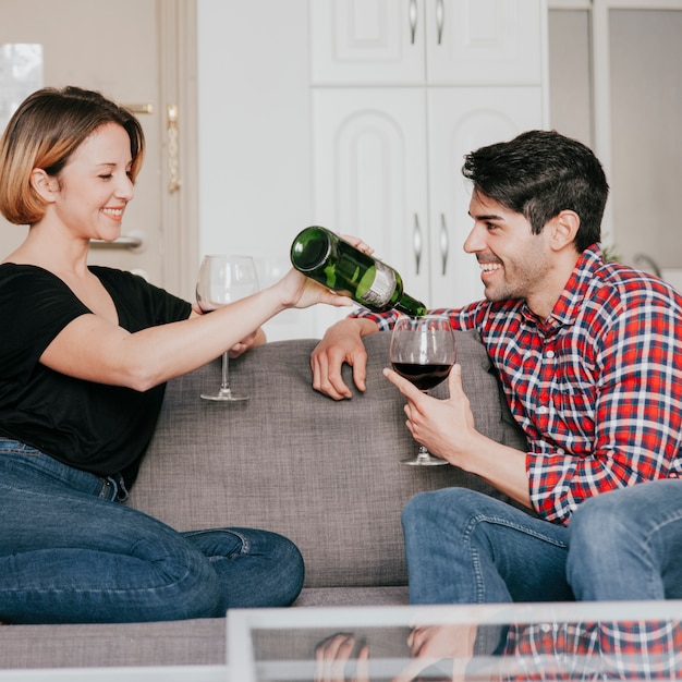 Foto gratuita pareja alegre vertiendo vino en el sofá