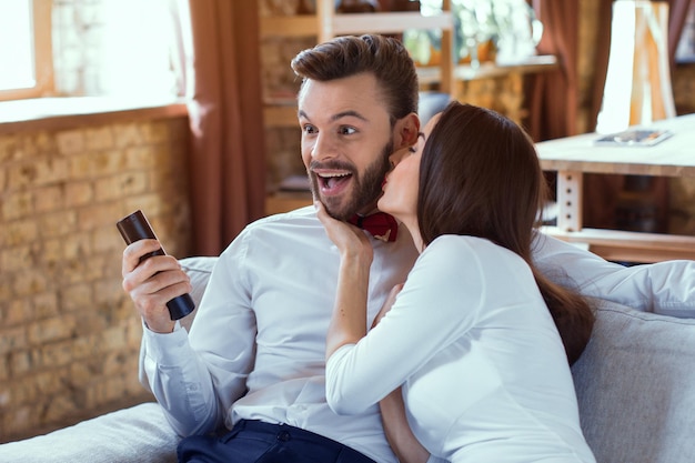 Pareja alegre viendo la televisión. Hermosa mujer besando al hombre en el sofá en la sala de estar.