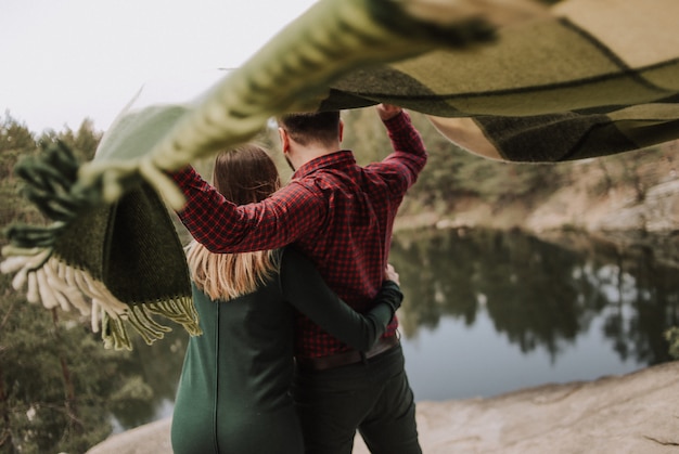 pareja amorosa con una alfombra desarrollándose en el viento en la orilla de un lago con un acantilado