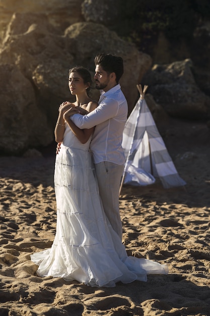 Pareja amorosa caucásica vistiendo ropa blanca y abrazándose en la playa durante una sesión de fotos de boda