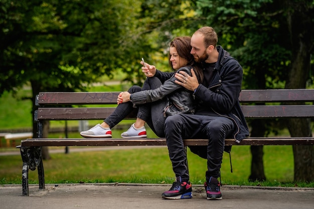 Una pareja amorosa de hombres barbudos y lindas mujeres morenas relajándose en un banco en un parque de otoño.