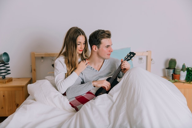 Pareja amorosa jugando ukelele en la cama