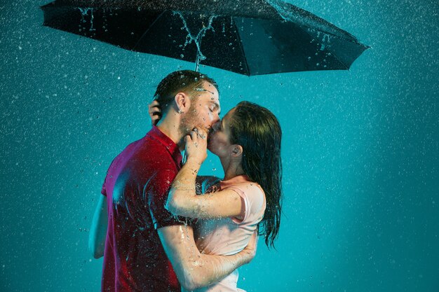 La pareja amorosa bajo la lluvia con paraguas sobre un fondo turquesa