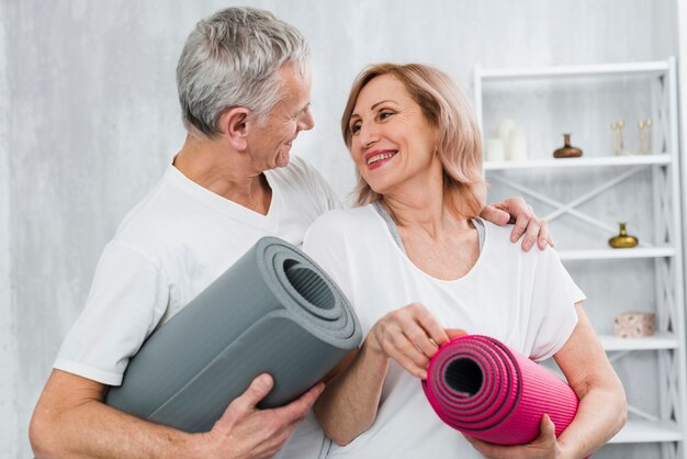 Pareja amorosa sosteniendo la estera de yoga mirando el uno al otro