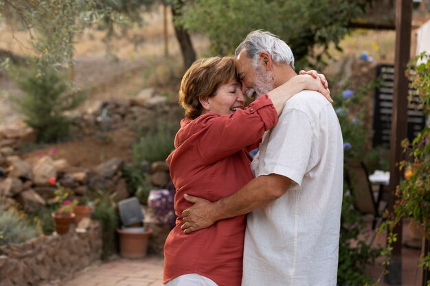 Una pareja de ancianos abrazándose románticamente en el jardín de su casa rural