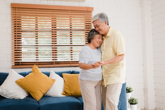 Pareja de ancianos asiáticos bailando juntos mientras escuchan música en la sala de estar en casa, dulce pareja disfruta el momento de amor mientras se divierte cuando se relaja en casa