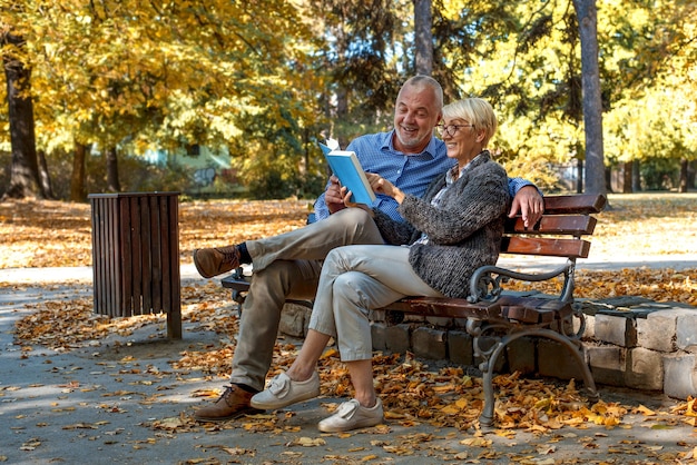 Pareja de ancianos caucásicos sentado en un banco y leyendo un libro en el parque