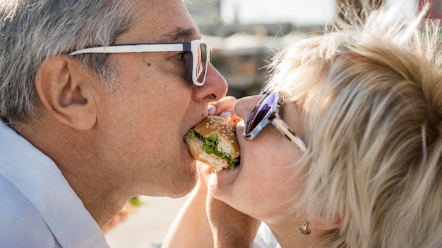 Pareja de ancianos compartiendo una hamburguesa al aire libre