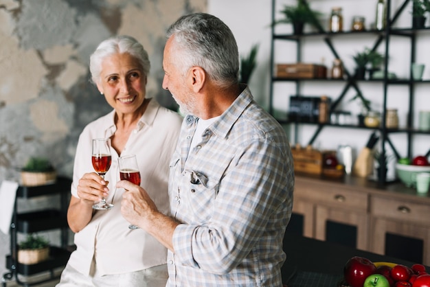 Foto gratuita una pareja de ancianos con copa de vino de pie en la cocina