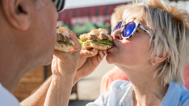 Pareja de ancianos disfrutando de comer una hamburguesa al aire libre