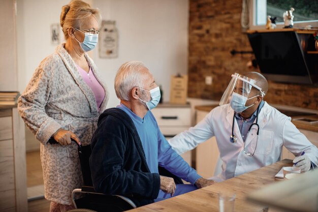 Pareja de ancianos hablando con un médico afroamericano que los visita durante la pandemia del coronavirus