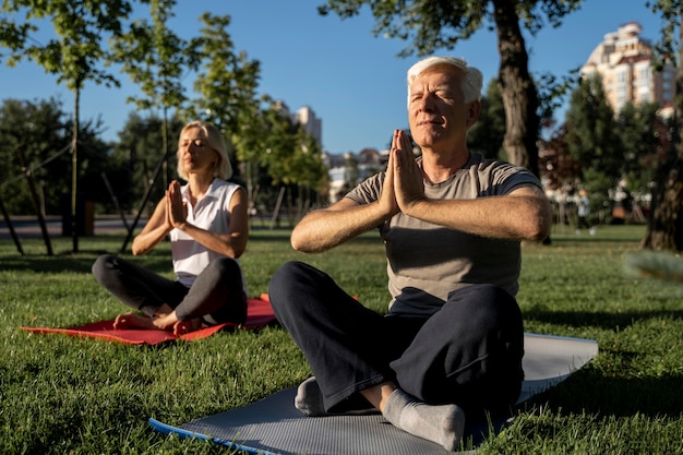 Pareja de ancianos haciendo yoga al aire libre