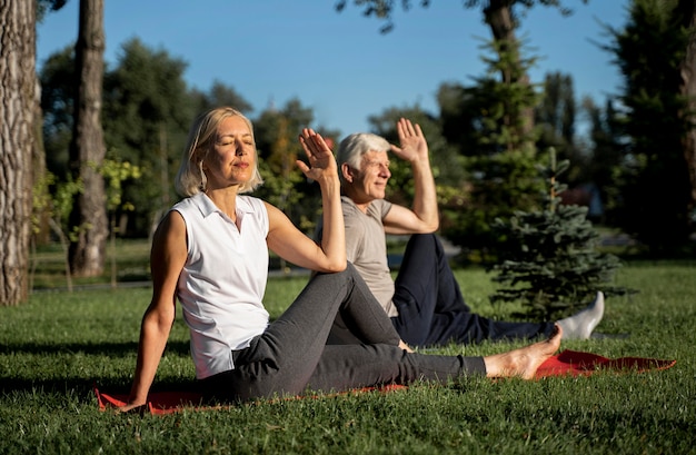 Pareja de ancianos haciendo yoga al aire libre