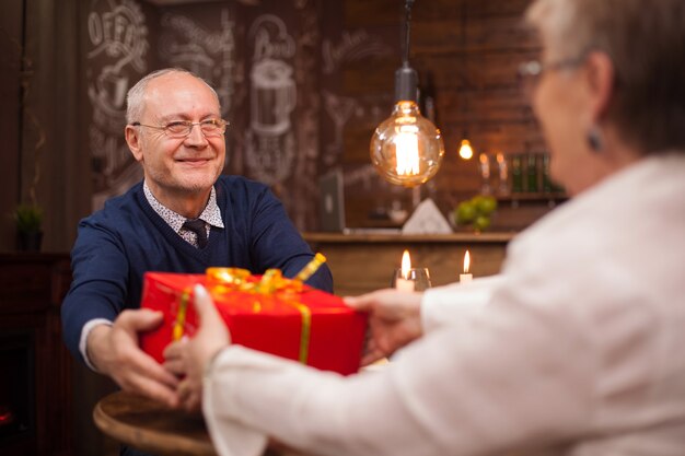 Pareja de ancianos jubilados pasando un buen rato durante la cena. Marido dando un regalo a su esposa.