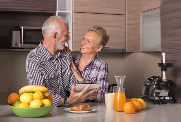 Pareja de ancianos jubilados viendo un video juntos en una tableta en una cocina