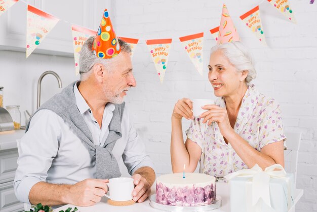 Pareja de ancianos mirándose mientras se toma una taza de café durante la fiesta de cumpleaños