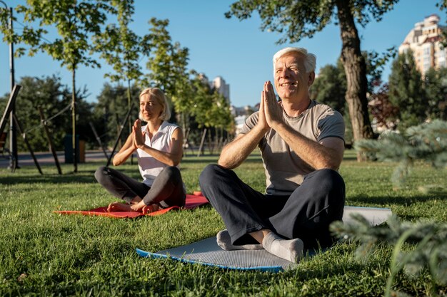 Pareja de ancianos practicando yoga fuera