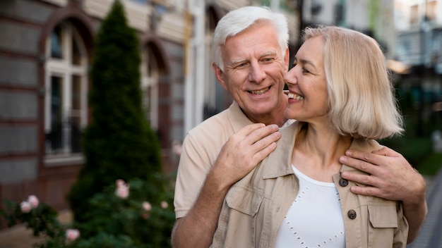 Pareja de ancianos sonrientes posando juntos mientras dan un paseo por la ciudad