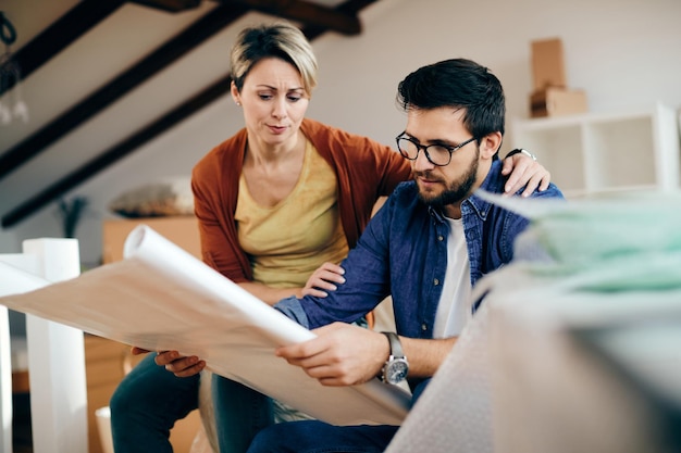 Pareja angustiada examinando los planes de vivienda de su nuevo hogar