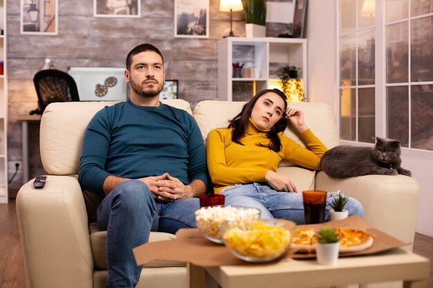 Pareja animando a su equipo favorito mientras ve la televisión y come comida rápida