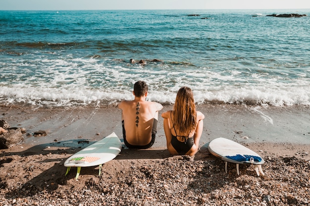 Foto gratuita pareja anónima con tablas de surf mirando al mar agitando